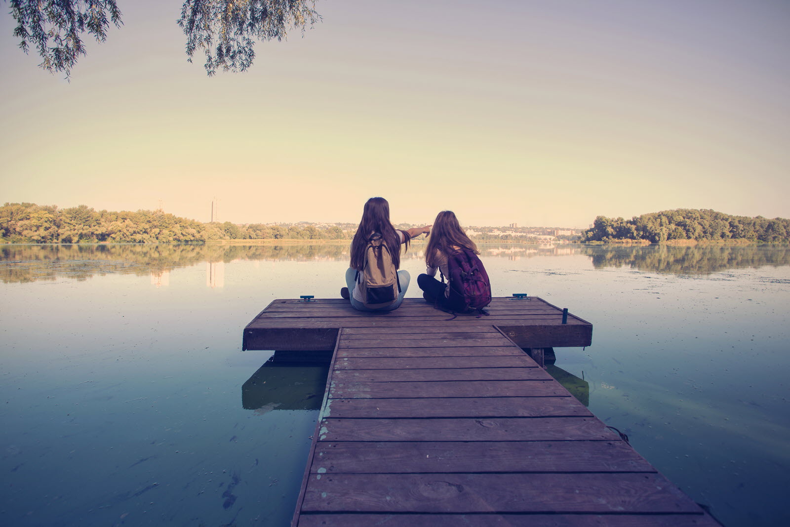 Two teenagers sitting on a pier looking out over a lake