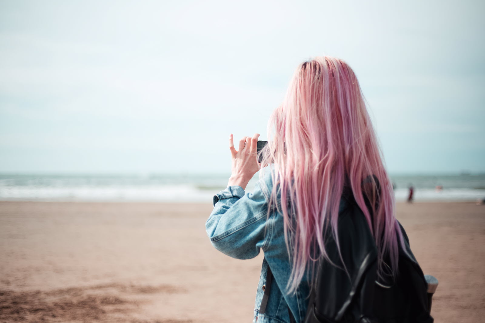 Pink-haired woman on beach taking photo of shoreline