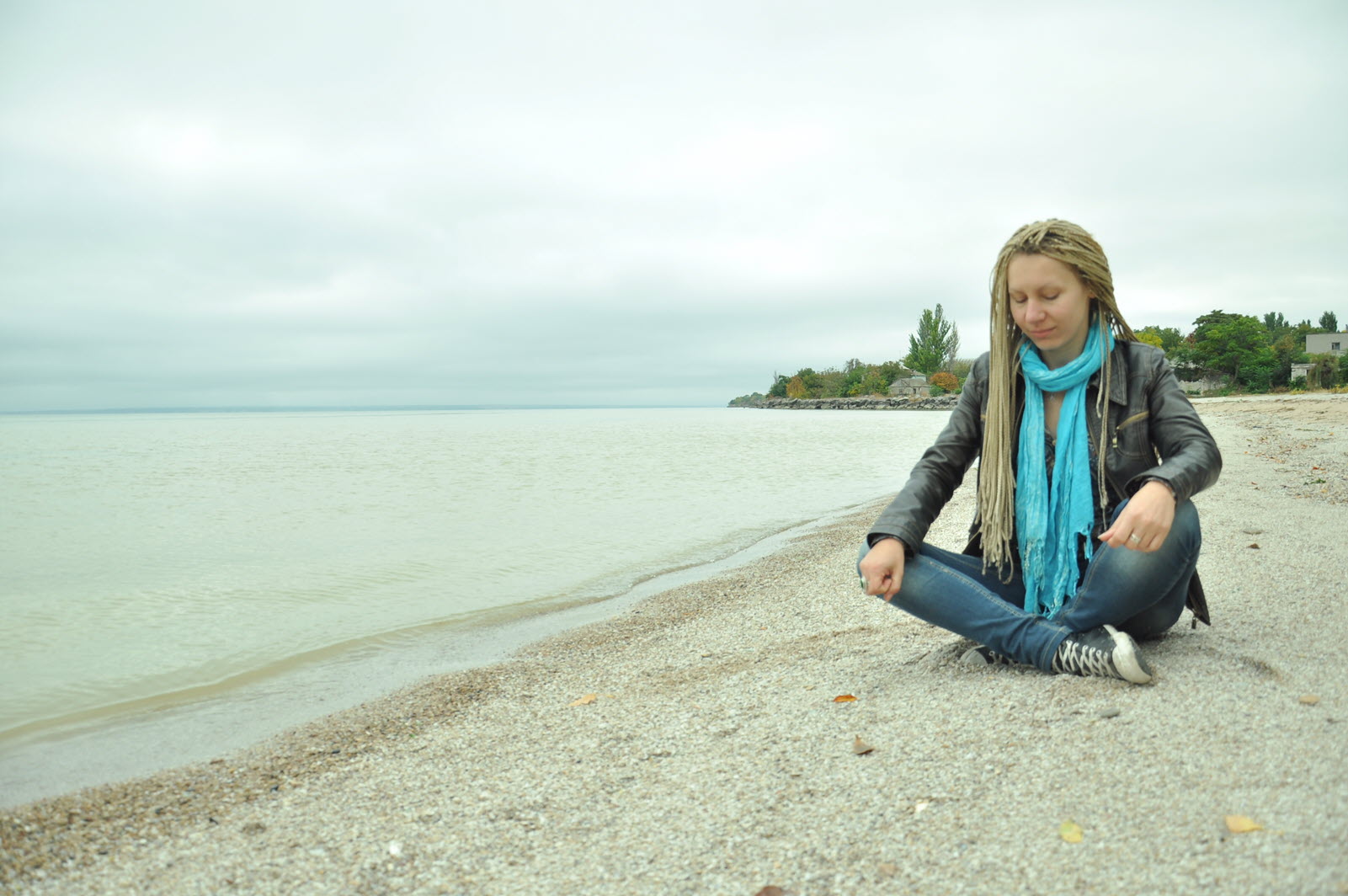 Woman with dreadlocks sitting cross-legged on a beach near the water